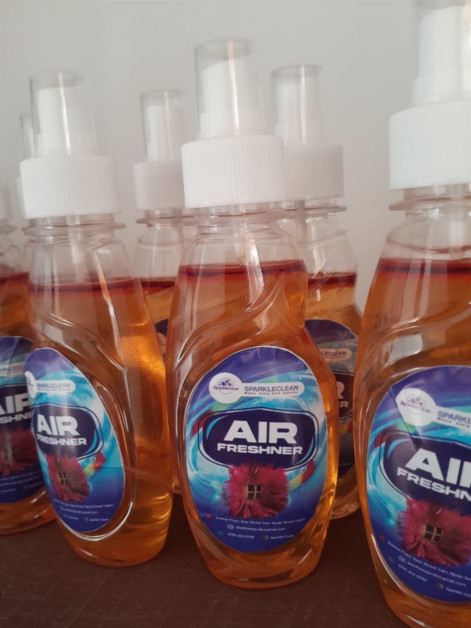 Several clear spray bottles with amber liquid, white pumps, and SparkleClean Air Freshner labels.