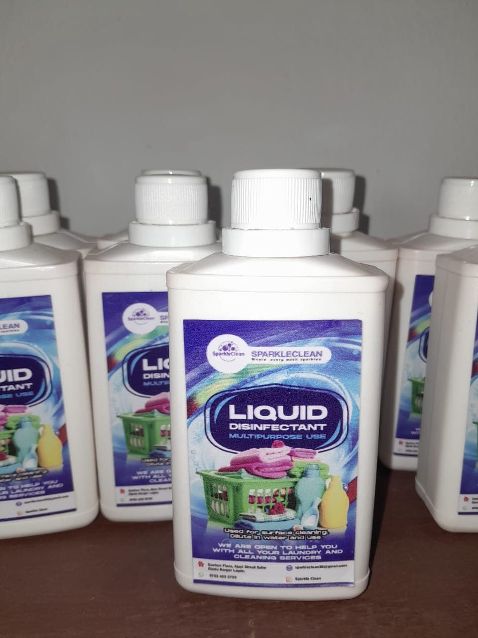 White plastic bottles of SparkleClean multipurpose liquid disinfectant arranged in rows on a surface.