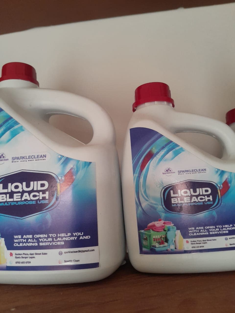 Two white jugs of SparkleClean multipurpose liquid bleach with red caps and blue labels.