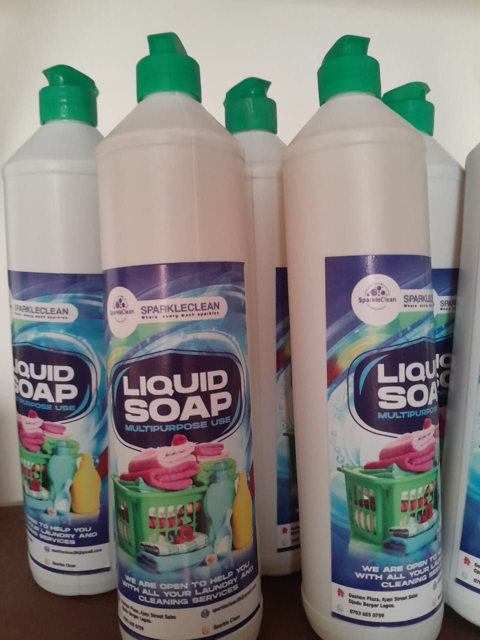 Multiple white bottles of SparkleClean multipurpose liquid soap with green caps and laundry-themed labels.