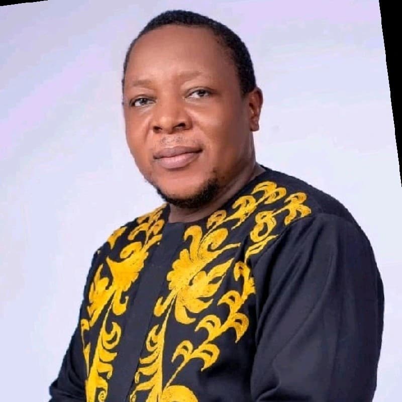 Man with a goatee wearing a black shirt with intricate yellow embroidery against plain background.